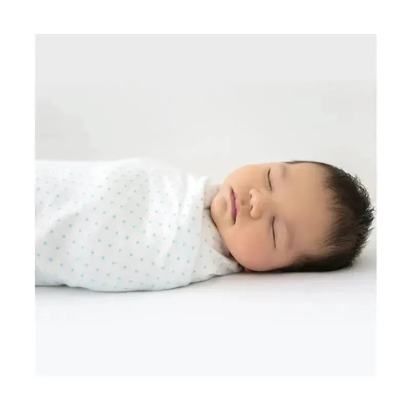 A sleeping baby swaddled in a pastel blue polka dot blanket, lying on a white surface.