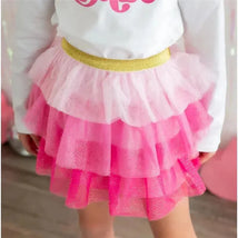 Kids pink petal tutu with layered ruffles, featuring a gold waistband and sparkly tulle, styled with a white long-sleeve shirt.