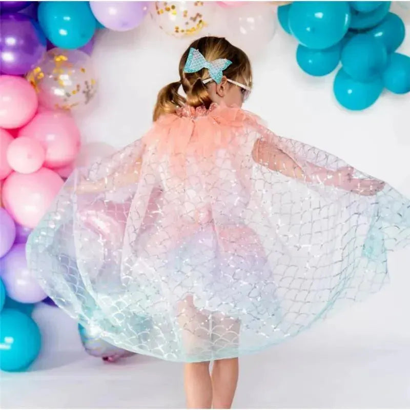 Kids summer mermaid bow clip worn by a girl with a colorful sheer cape, surrounded by balloons.