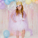 A girl wears a lavender dress-up kit featuring a sparkly cape and heart-shaped sunglasses, posing confidently against a colorful backdrop.