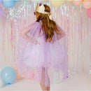 Child wearing a lavender dress up kit with a sparkling cape and crown, surrounded by pastel balloons and a festive backdrop.