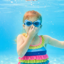 Child wearing Swimways Bluey swim goggles, underwater, holding her nose, in a colorful striped swimsuit.