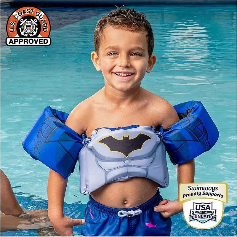 Smiling boy wearing a SwimWays Swim Trainer Life Jacket featuring a Batman design, standing in a pool.