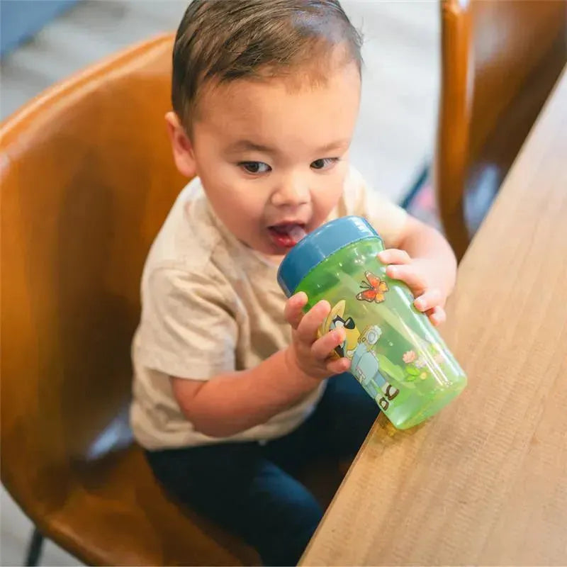 Child seated at a table holding a 12 oz Bluey Baby Straw Cup with colorful designs, enjoying a drink.