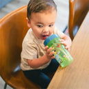 Child seated at a table holding a 12 oz Bluey Baby Straw Cup with colorful designs, enjoying a drink.
