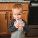 A child drinks from a Bluey Take & Toss straw cup, featuring colorful designs, while standing in a kitchen.