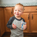 Smiling toddler holding a Bluey Take & Toss Straw Cup with colorful graphics, standing in a kitchen.
