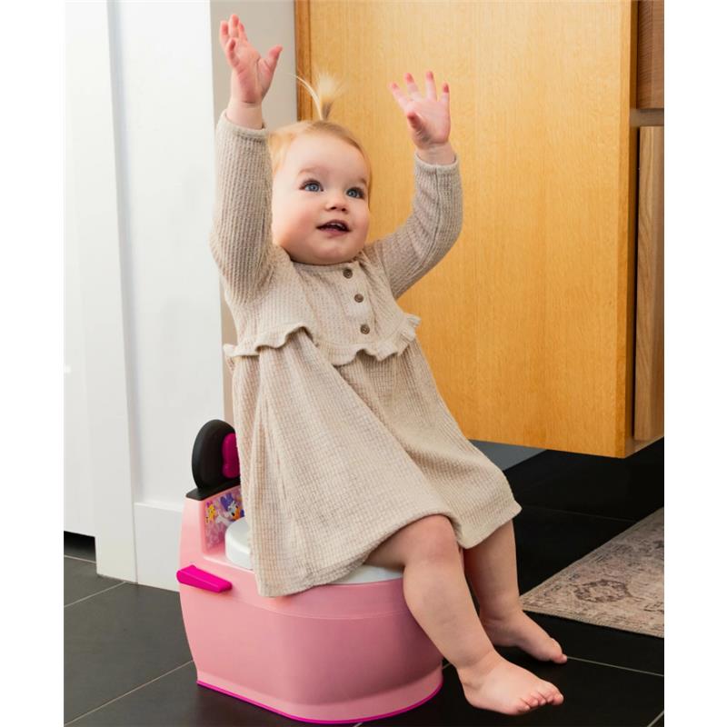 Toddler sitting on The First Years Minnie 2 In 1 Potty, smiling with arms raised, wearing a long beige dress.
