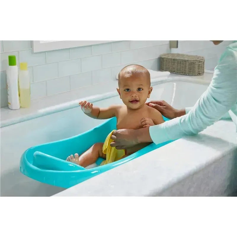 Newborn in a blue 3-in-1 baby bathtub, smiling while an adult assists with a towel in a bright bathroom.