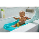Newborn in a blue 3-in-1 baby bathtub, smiling while an adult assists with a towel in a bright bathroom.