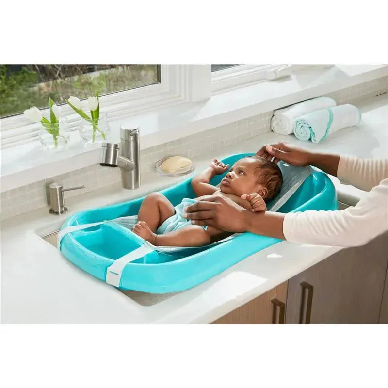 3-in-1 baby bathtub in blue with a baby lying inside, being held by a caregiver at a sink.