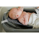 Newborn resting on a grey baby bathtub with a polka dot support pad, preparing for a bath.