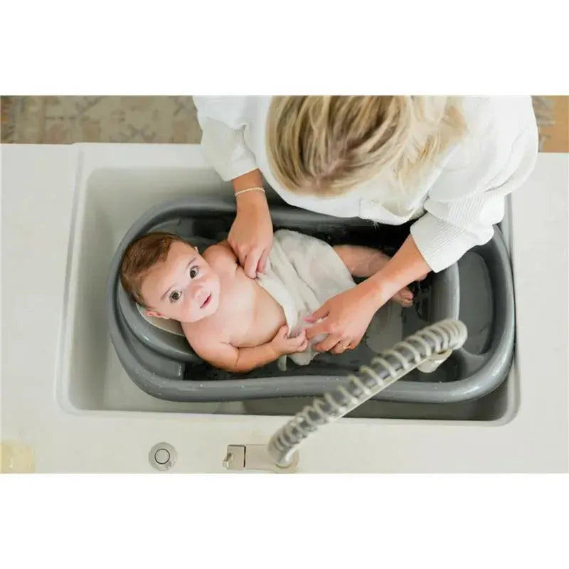Baby comfortably sitting in a grey 3-in-1 bathtub while an adult dries them with a towel.