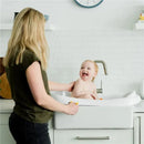 Baby enjoying a bath in the Sure Comfort® 3-in-1 Baby Bathtub, held by a caregiver in a modern kitchen setting.