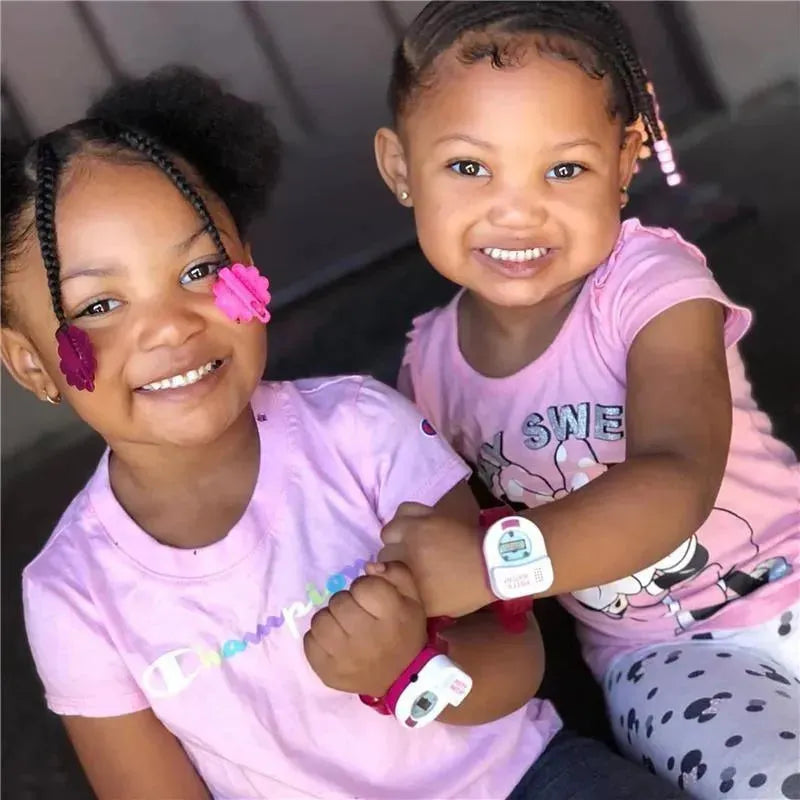 Two smiling girls wearing matching pink shirts, each sporting a colorful Original Potty Watch on their wrists.