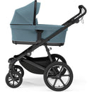 Thule Bassinet Mid in blue, featuring a spacious fabric enclosure on a sturdy stroller frame with large wheels.