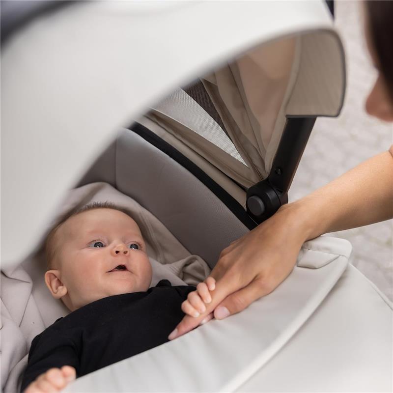 Thule Bassinet Mid in blue with a baby lying inside, looking up at a hand gently holding theirs.