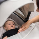 Thule Bassinet Mid in blue with a baby lying inside, looking up at a hand gently holding theirs.