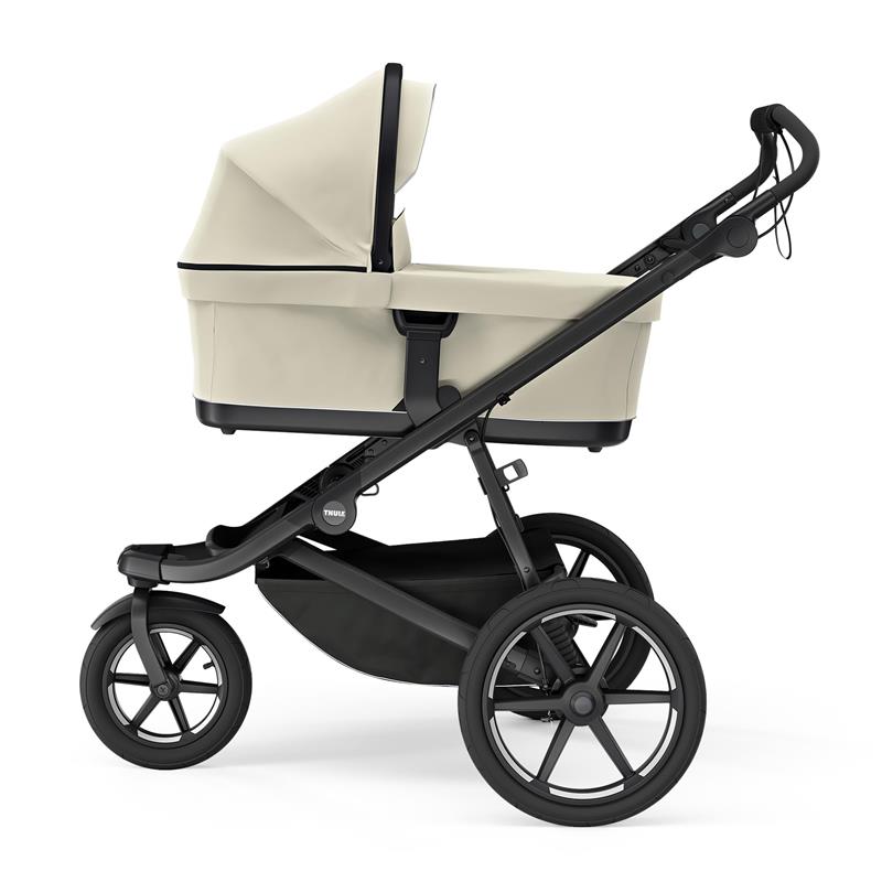 Soft beige Thule bassinet attached to a stroller frame, showcasing its sleek design and large wheels.