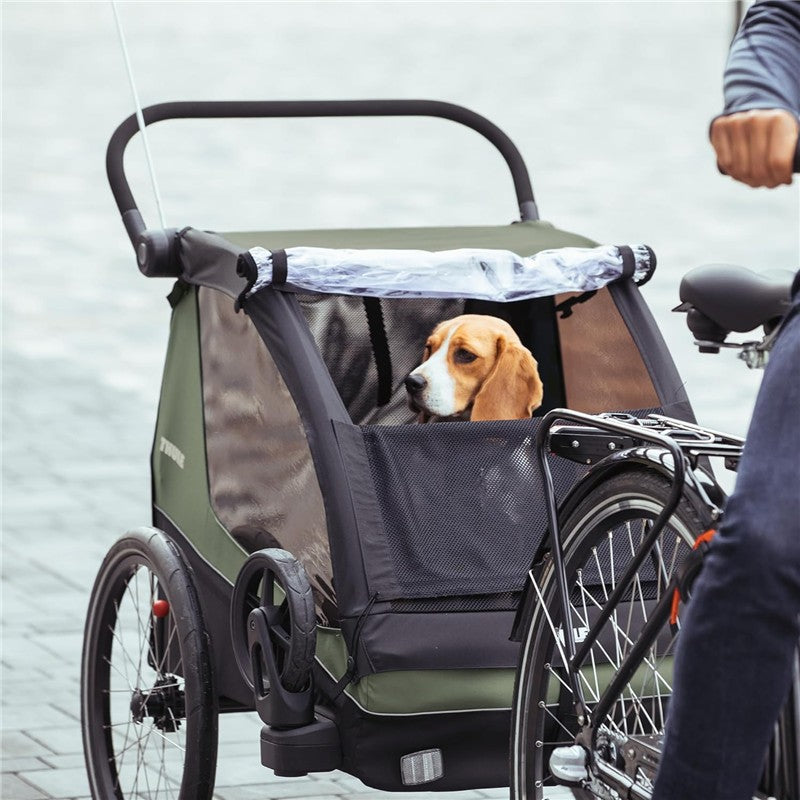 Thule Courier Child Bike in Vintage Green with a beagle inside, parked beside a bicycle on a paved surface.