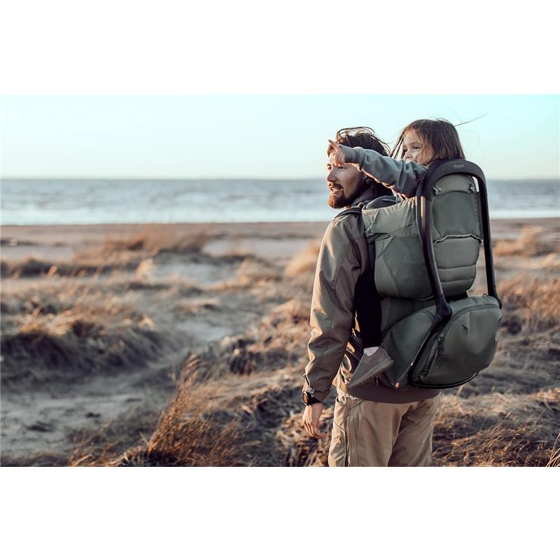 Child enjoys a scenic view from the Thule Sapling Child Carrier Backpack, worn by an adult on a beach.