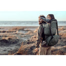 Child enjoys a scenic view from the Thule Sapling Child Carrier Backpack, worn by an adult on a beach.