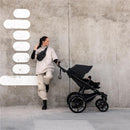 Single child all-terrain stroller in black, with a female user leaning against a textured wall.