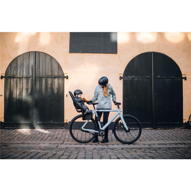 Mother and child in helmets by a bike with a Thule Yepp 2 Maxi frame-mount seat, set against rustic black doors.