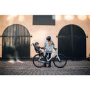 Mother and child in helmets by a bike with a Thule Yepp 2 Maxi frame-mount seat, set against rustic black doors.