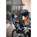 Child seated in Thule Yepp 2 Maxi bike seat, wearing a helmet and winter attire, with caregiver adjusting the seat.