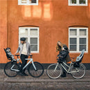 A man and woman stand beside bicycles on a cobblestone street, with a child seated in a Thule Yepp Maxi child seat on each bike.