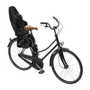 Child bike seat mounted on a black bike, featuring a padded wooden seat and adjustable harness for safety.