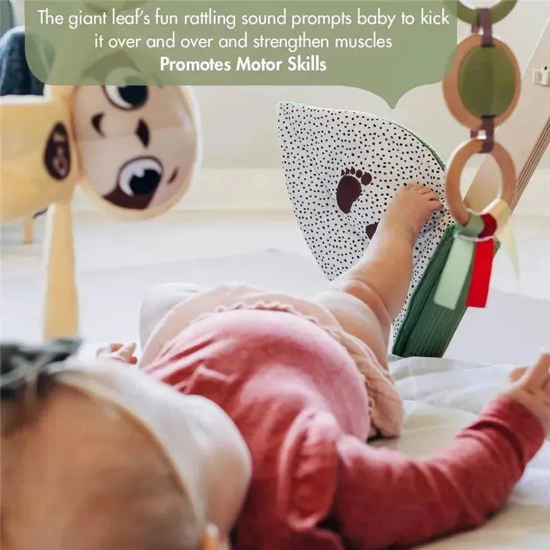 Baby lying on a Tiny Love Boho Chic Gymini Play Mat, interacting with a colorful hanging toy and a giant leaf design.