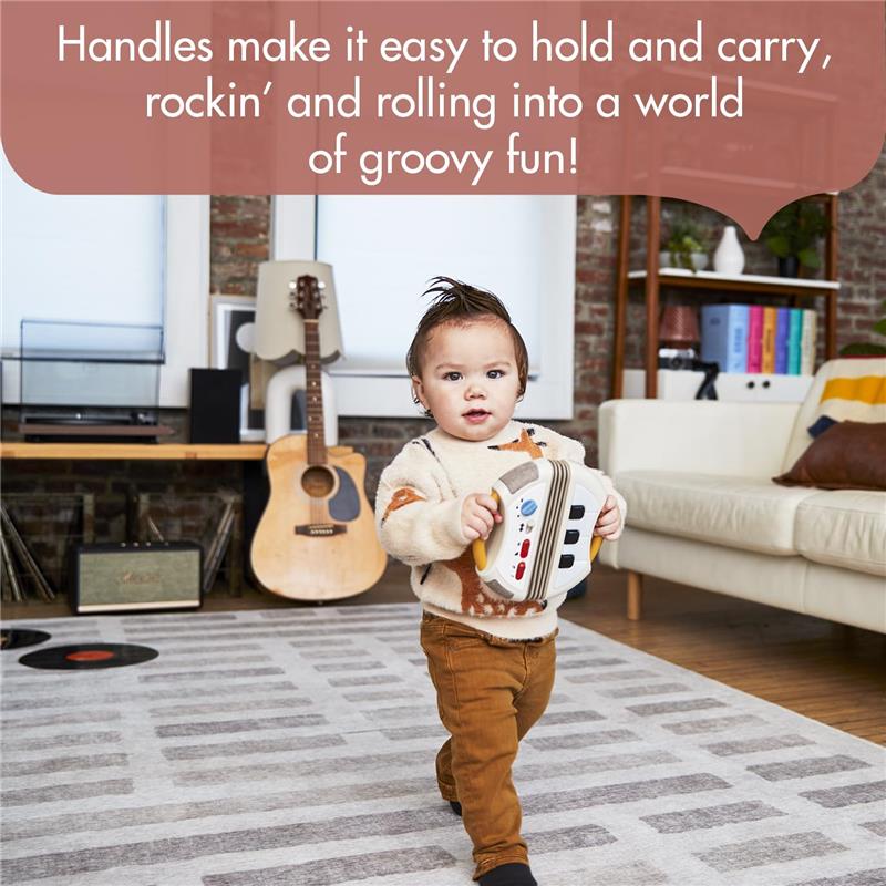 A toddler holds the Tiny Love Tiny Rockers Accordion Toy, smiling and walking in a cozy living room with musical instruments.