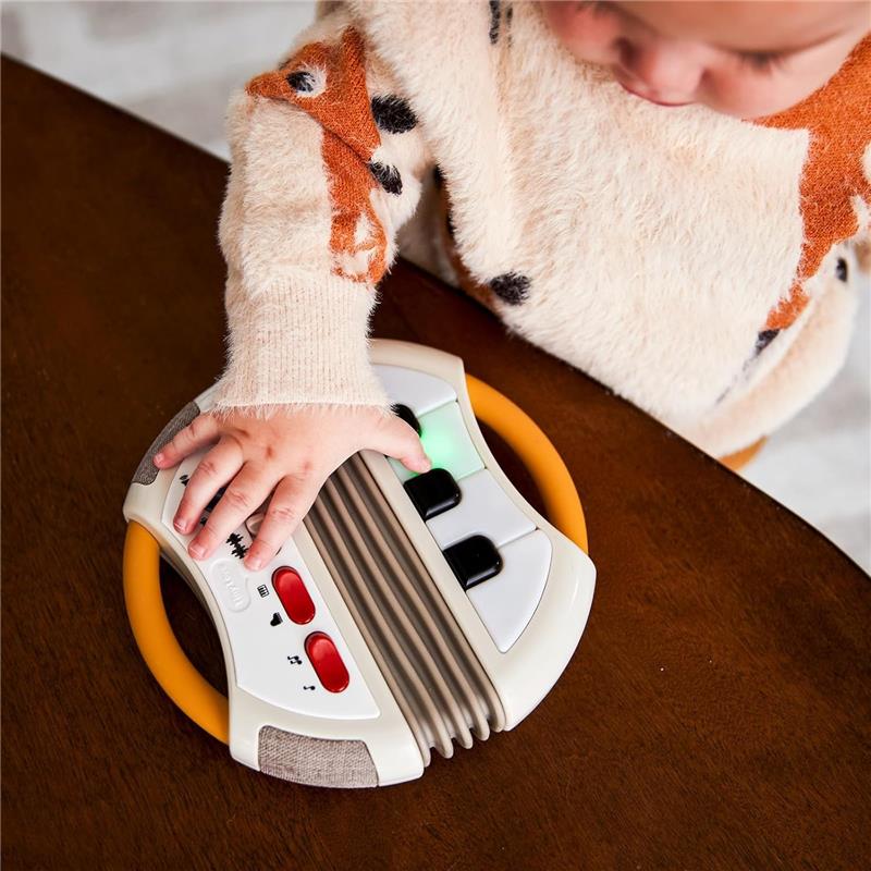 A child’s hand touches the Tiny Love Tiny Rockers Accordion Toy, featuring colorful buttons and keys, on a wooden surface.