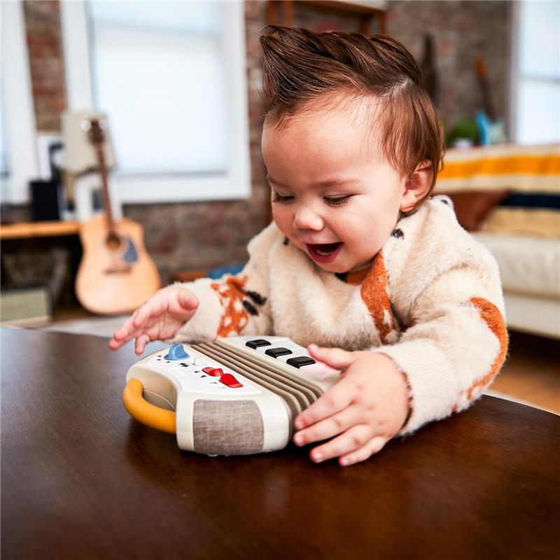 Toddler joyfully plays with a Tiny Love Accordion Toy featuring buttons and a handle on a wooden table.