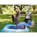 A woman joyfully lifts a baby while a child rests on a blue marine-themed picnic mat outdoors, with a stroller nearby.
