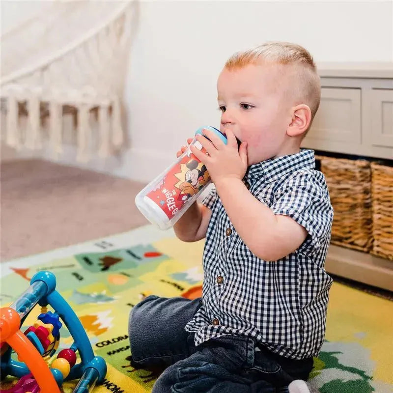 Child sitting on a colorful play mat, drinking from a Disney Mickey Mouse insulated sippy cup.