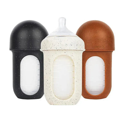 Three 8oz Tomy Nursh bottles in black, speckled white, and brown, designed for easy feeding. Each has a clear measurement window.