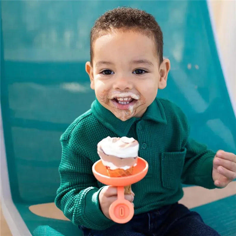 Young child with a slight smile holds a Tomy Boon Drizzle Popsicle Holder featuring an ice cream cone, enjoying a treat.