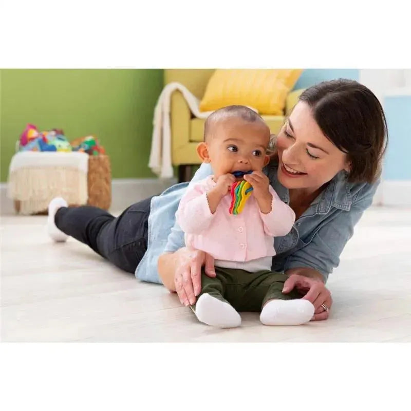 Baby playing with colorful Tomy Lamaze My First Keys toy while lying on the floor with a smiling woman.