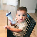 Toddler holding a Bluey insulated sippy cup featuring a playful character design, sitting at a wooden table.