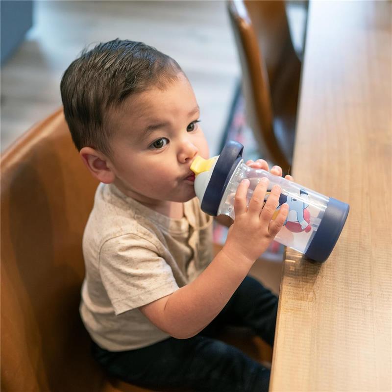 Toddler drinks from a blue water bottle with a straw, featuring a colorful design, sitting at a wooden table.