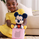 Cuddle Mickey Mouse plush toy sits on a pink audio speaker held by a smiling child wearing a yellow dress.
