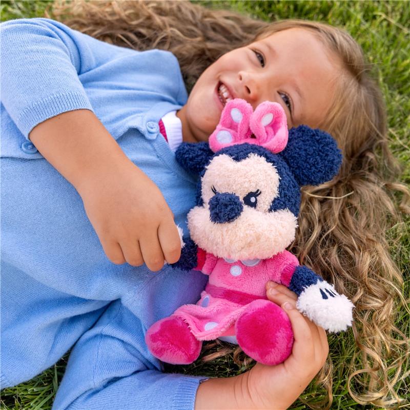Cuddle Minnie Mouse plush toy held by a smiling girl in a blue cardigan, lying on green grass.