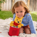 Tonies Cuddle Winnie the Pooh plush toy with a child, seated on a blanket outdoors, enjoying audio storytelling.