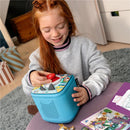 Girl with long red hair plays with Tonies Lalalinos Find The Photo game on a blue device, pressing a red button while smiling.