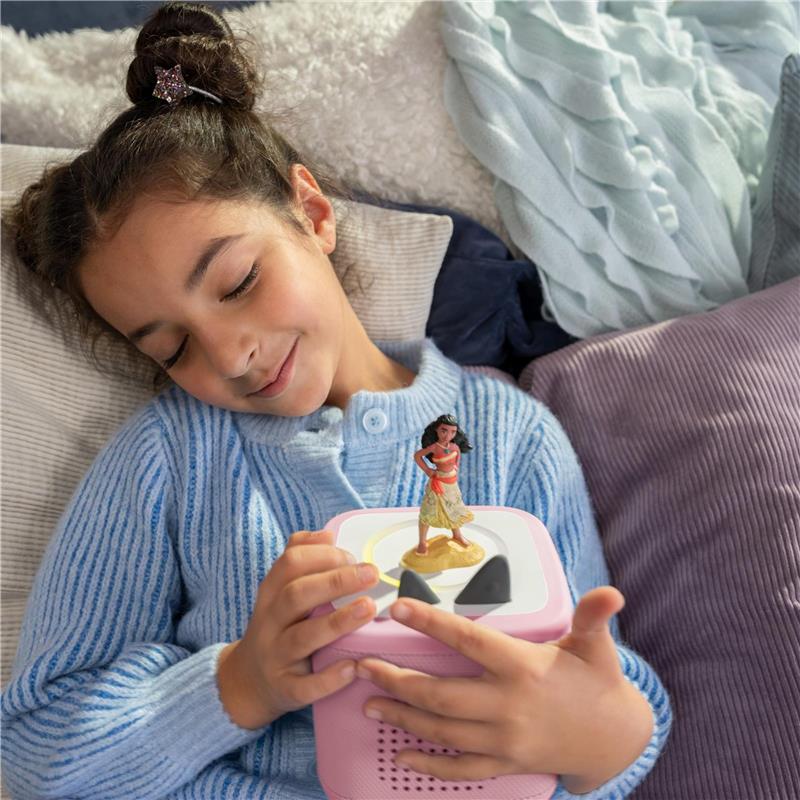 A young girl in a blue sweater smiles while holding a pink Tonies audio box featuring a Moana figurine on top.