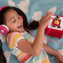 Girl wearing pink headphones joyfully interacts with a red Tonies Mulan Audio Toy Figurine while lying on a cloud-patterned blanket.