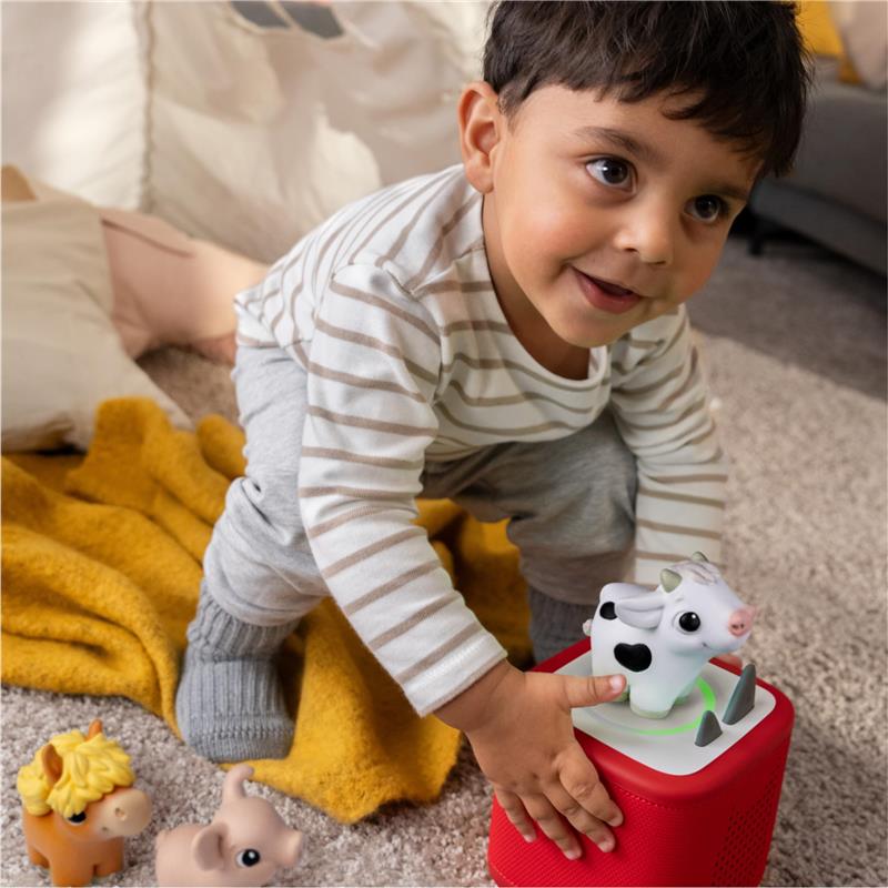 Soft and squeezable cow, pig, and horse figurines by Tonies, with a toddler playing and smiling in a cozy setting.